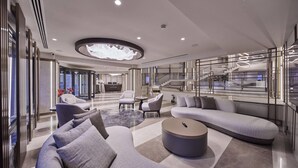 A modern hotel lobby with a curved sofa, a round coffee table, and a reception desk.