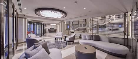 A modern hotel lobby with a curved sofa, a round coffee table, and a reception desk.