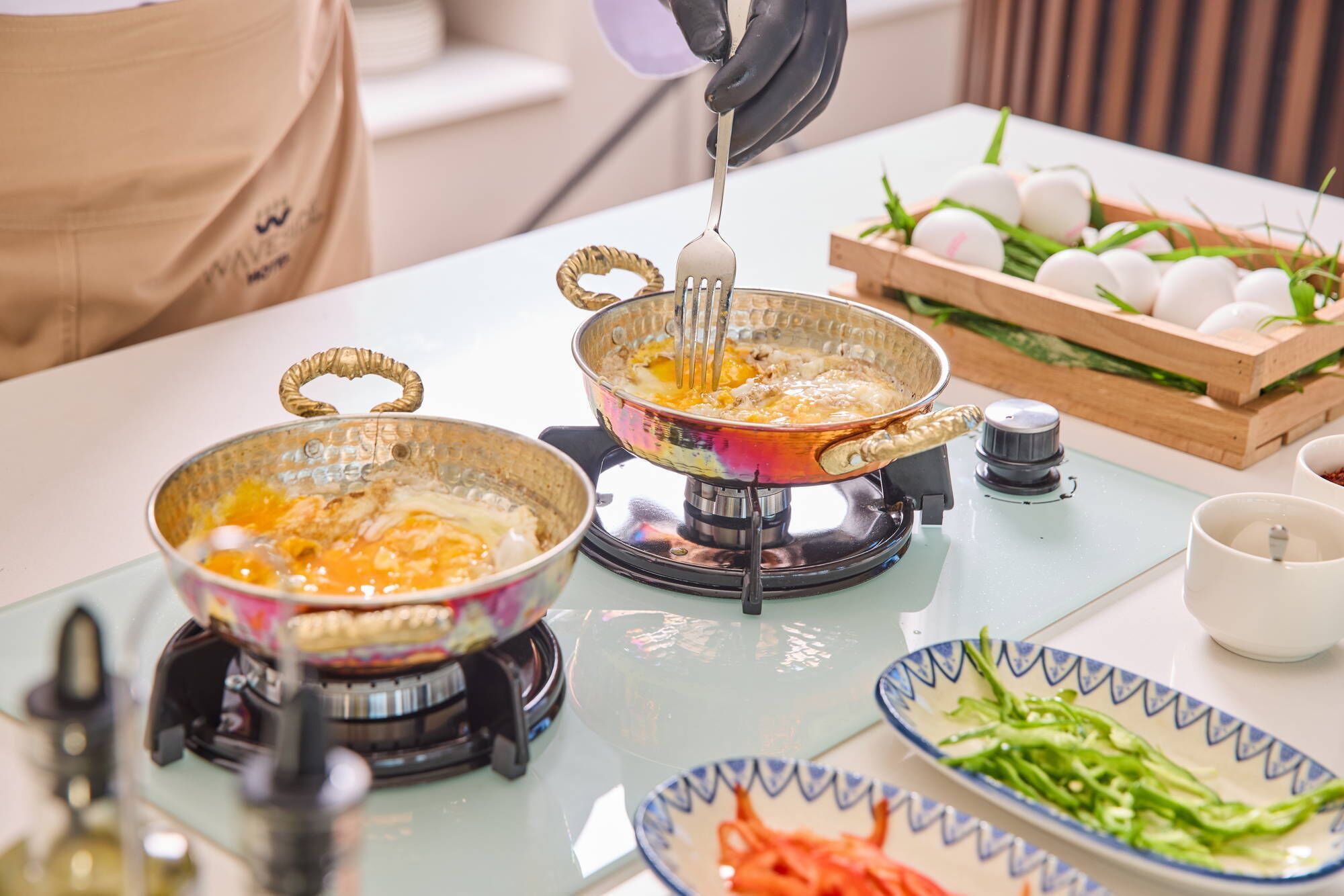 A kitchen with two electric griddles, a bowl of eggs, and a tray of vegetables.