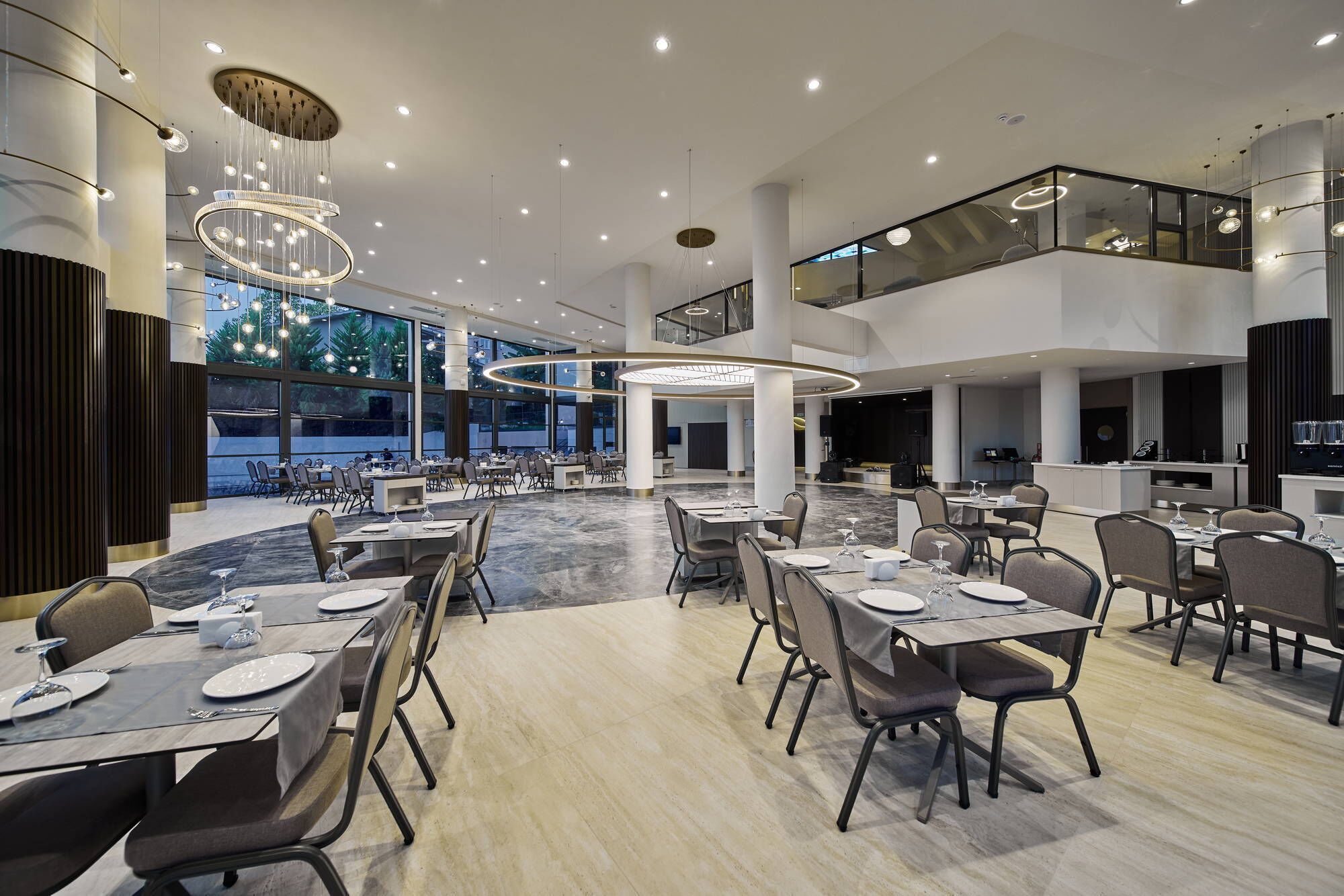 A modern dining area with multiple tables, overhead lighting, and large windows.