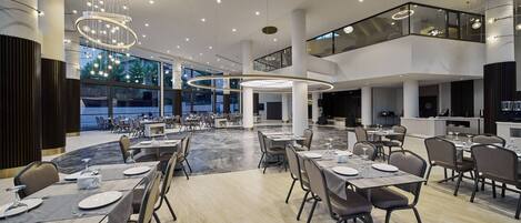 A modern dining area with multiple tables, overhead lighting, and large windows.