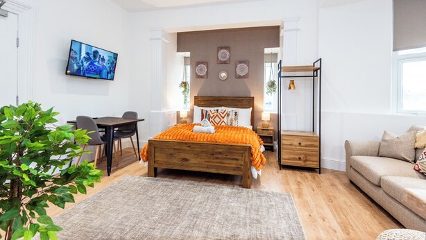 A bedroom with a bed, bedside tables, a TV, a desk, and a sofa. - Glan Neigr by Guestz (Rhosneigr)