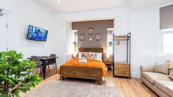 Un dormitorio con cama, mesitas de noche, televisor, escritorio y sofá.