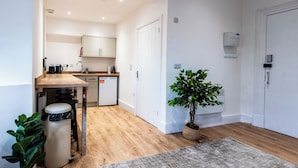 A compact kitchen with wooden flooring, a coffee machine, a dishwasher, and a potted plant. - Glan Neigr by Guestz (Rhosneigr)