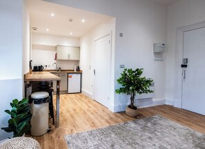 A compact kitchen with wooden flooring, a coffee machine, a dishwasher, and a potted plant. - Glan Neigr by Guestz (Rhosneigr)