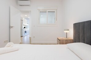 Una camera da letto con un letto, un comodino con una lampada, una finestra e una porta che dà su una cucina.