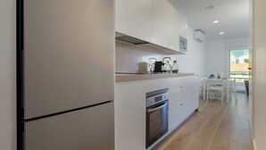 Et moderne køkken med hvide skabe, en indbygget ovn og et spiseområde med bord og stole.