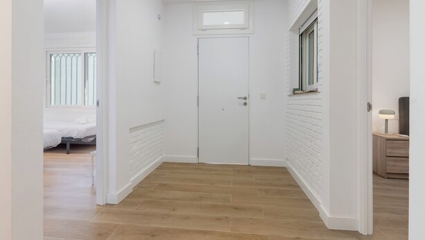 A hallway with a white door, wooden flooring, and a bed in the adjacent room. - Luxury apartment with terrace facing the sea (El Puerto de Santa María)