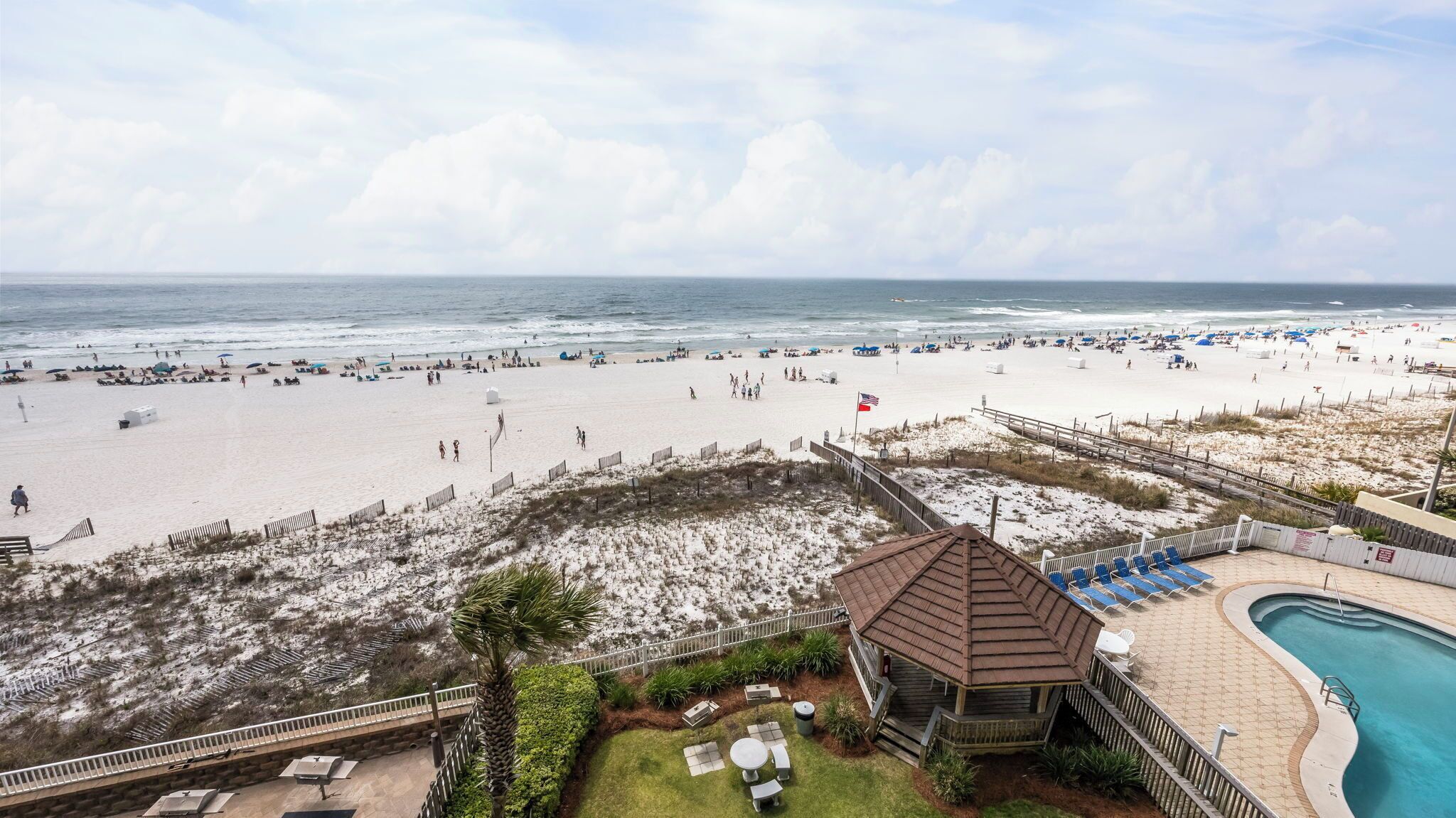 Vista de una playa con área de piscina, una torre de salvavidas y una playa de arena con sombrillas.