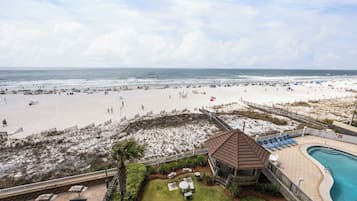 Vista de una playa con área de piscina, una torre de salvavidas y una playa de arena con sombrillas.