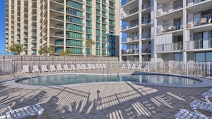 A swimming pool with sun loungers, surrounded by a fence, and a tall building in the background. - Gulf front 3BR corner unit with pool + Sleeps 7 (Orange Beach)