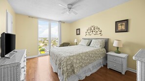 A bedroom with a bed, a television, wicker furniture, and a balcony with a view. - Gulf front 3BR corner unit with pool + Sleeps 7 (Orange Beach)