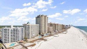 A beachfront hotel with multiple buildings, a sandy beach, and a clear sky. - Gulf front 3BR corner unit with pool + Sleeps 7 (Orange Beach)