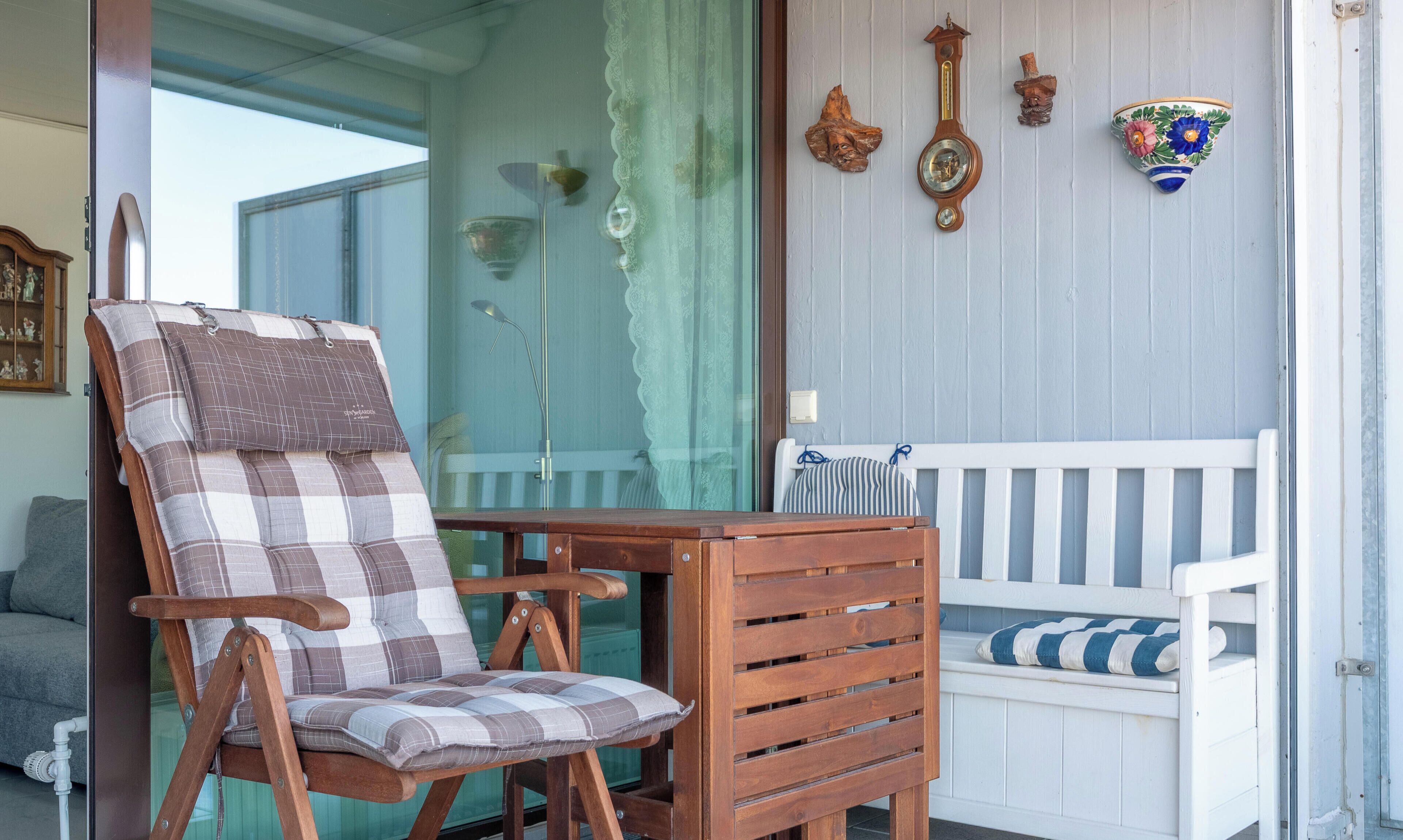 A wooden chair with a plaid cushion, a white bench with striped cushions, and decorative wall clocks.