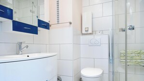 Ein modernes Badezimmer mit einem weißen Waschbecken, einem Spiegel, einer Toilette, einer Duschkabine aus Glas und einem Handtuchhalter.