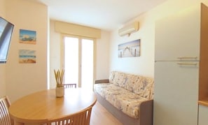 Ein kompakter Wohnbereich mit Sofa, Esstisch und Kühlschrank.