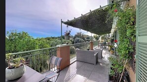 A balcony with outdoor furniture, a pergola, and a view of the surrounding greenery.
