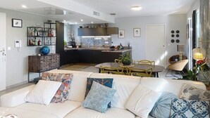 A modern living room with a sofa, a dining area, and a kitchen in the background.