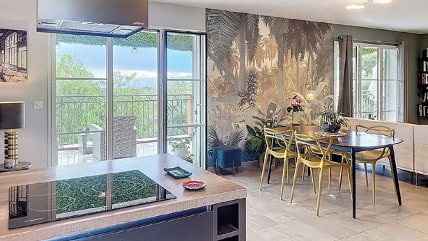 A modern kitchen with a large window, a dining area with yellow chairs, and a balcony with a view.