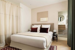A hotel room with a bed, a nightstand, a mirror, and a bathroom visible through an open door. - Marais Gem 2BR 6P Paris Stay (Paris)