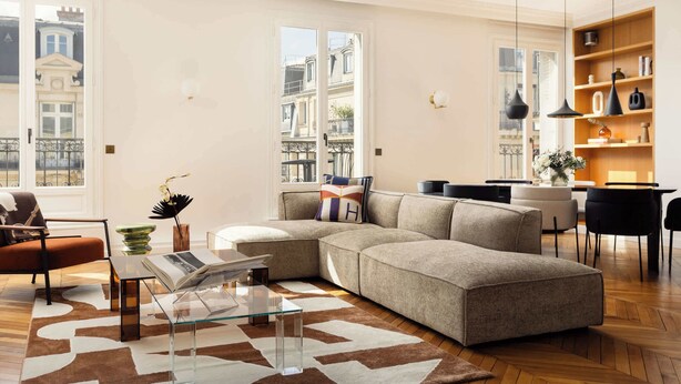 Una sala de estar moderna con un sofá seccional, una mesa de centro de vidrio y una zona de comedor con una silla negra.