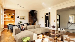 Una sala de estar moderna con un sofá modular, una mesa de centro de vidrio y un comedor con una silla y una pequeña mesa.