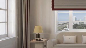 A room with a sofa, a small table, a lamp, and a view of a cityscape through a window. - Cipriani Punta Del Este  (Punta del Este)