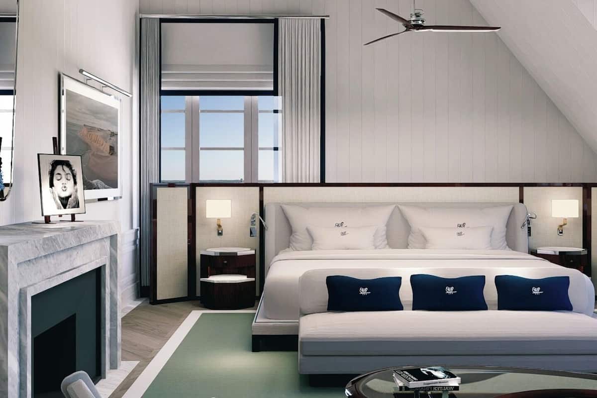 A modern hotel room with a large bed, a ceiling fan, a fireplace, and a view of the outdoors.