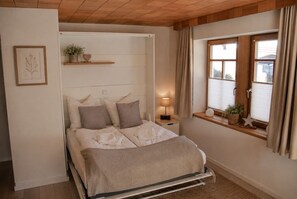 Una cama con cabecera, mesita de noche, lámpara y ventana con cortinas.