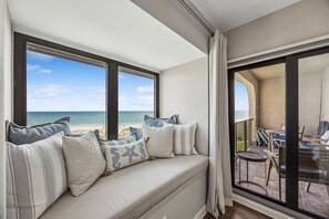A balcony with a view of the sea, a cushioned seating area with patterned cushions, and a table with chairs. - Oceanfront Turtle Dunes 5th Floor RENOVATED - Private Balcony - Beach & Pool! (Fernandina Beach)