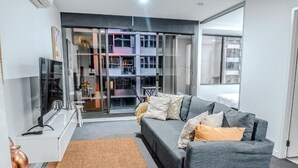 Een moderne woonkamer met een grijze bank, een flatscreen-tv en een glazen deur naar een balkon.