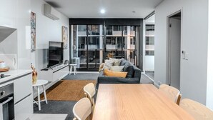Een moderne leefruimte met keuken, eethoek en zithoek, met een groot raam, inbouwapparatuur en een flatscreen-tv.