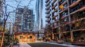 Een modern woongebied in de stad met hoge gebouwen, een open ruimte in het midden met zitplaatsen en een verzorgd gazon.