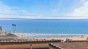 Vista da praia com céu claro, areia dourada e um edifício com uma bandeira.