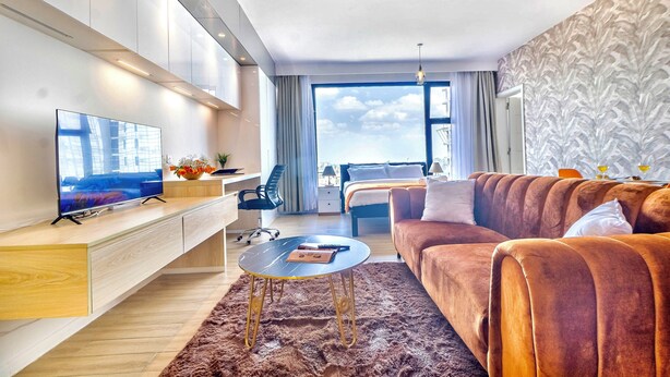 A modern hotel room with a flat-screen TV, a sofa, a bed, a desk, and a large window offering a city view. - Cozy studio apartment in lovely Nairobi with amazing city views (Nairobi)