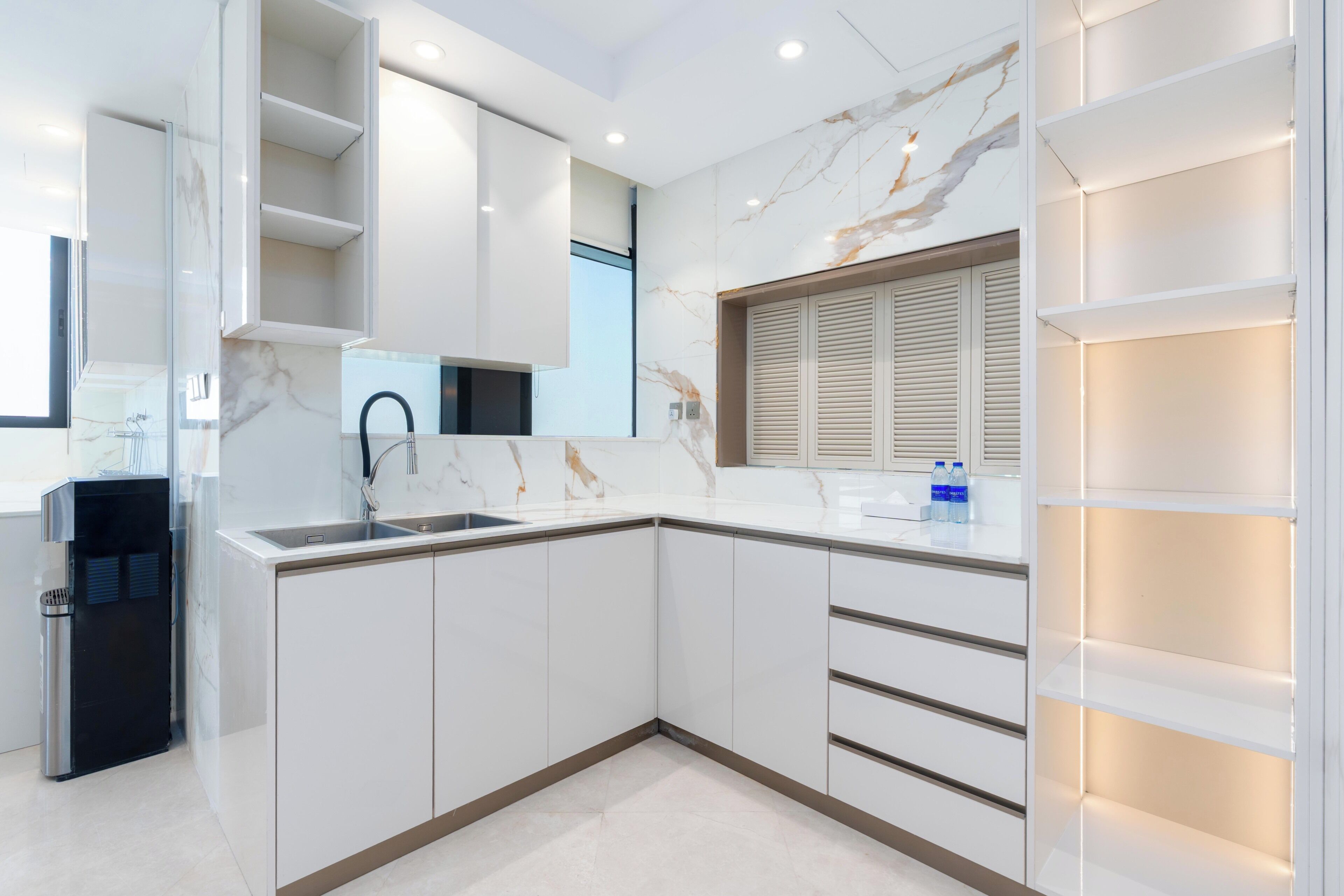 A modern kitchen with white cabinetry, a marble backsplash, and built-in shelves.
