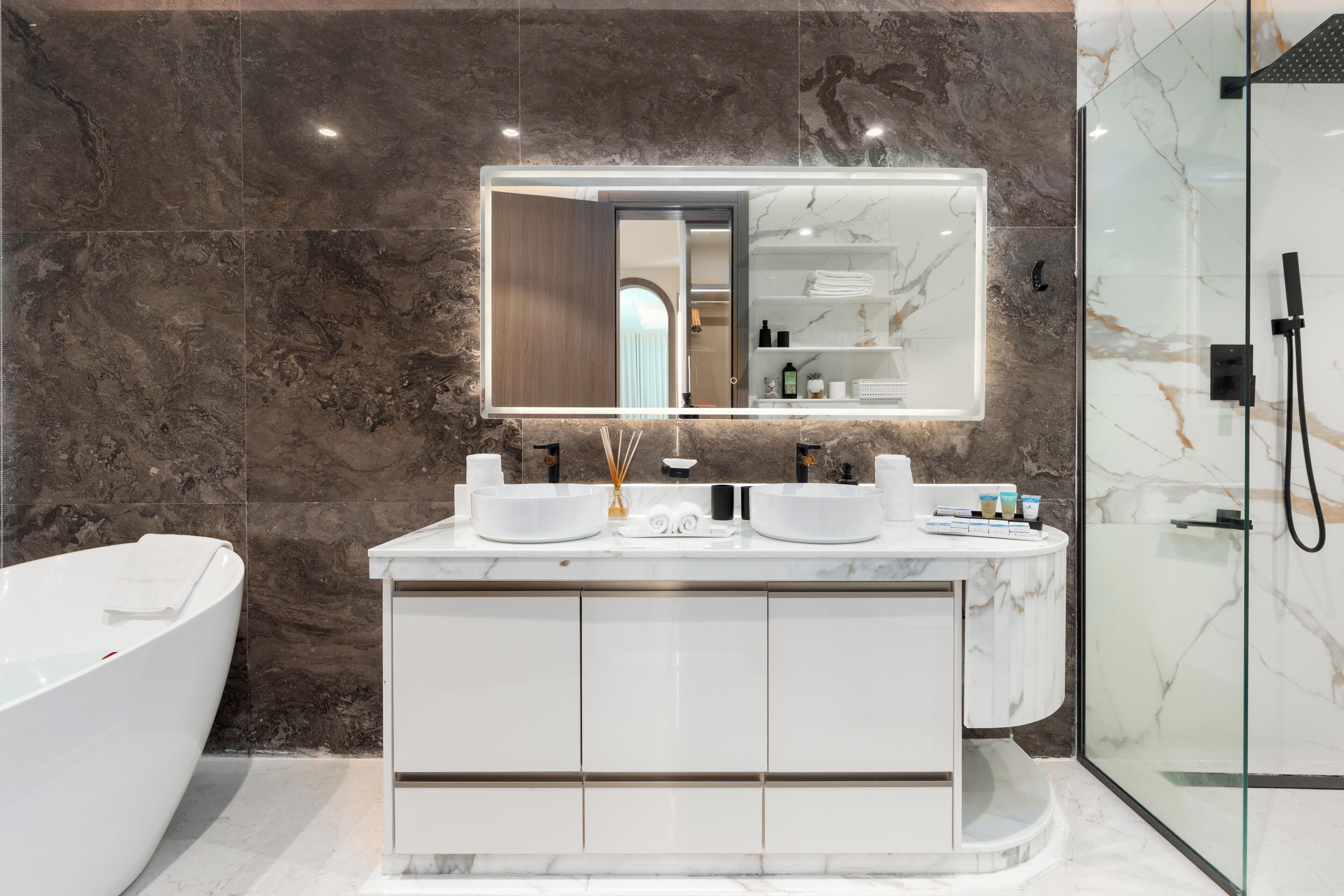 Une salle de bain moderne avec un grand miroir, deux lavabos, une baignoire et une douche à l’italienne.