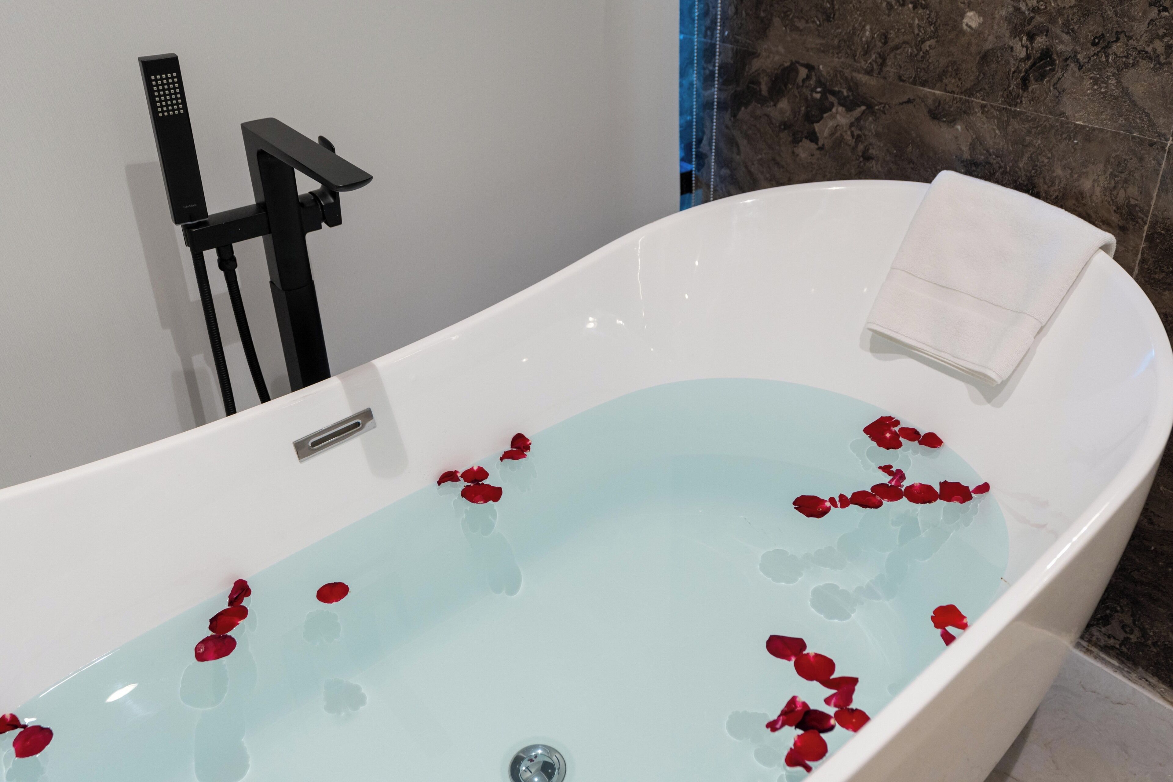 A bathtub with rose petals, a towel, and a showerhead.