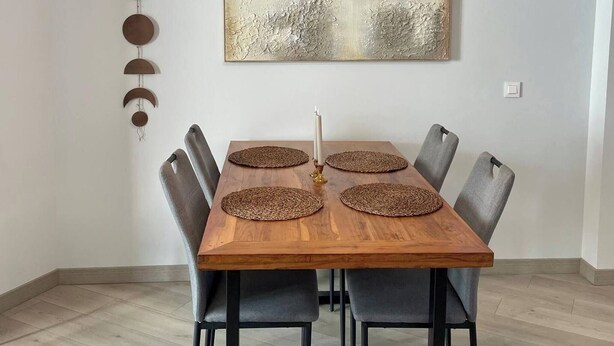 Ein Essbereich mit Holztisch, grauen Stühlen, einer modernen Pendelleuchte und einem strukturierten, abstrakten Gemälde an der Wand.
