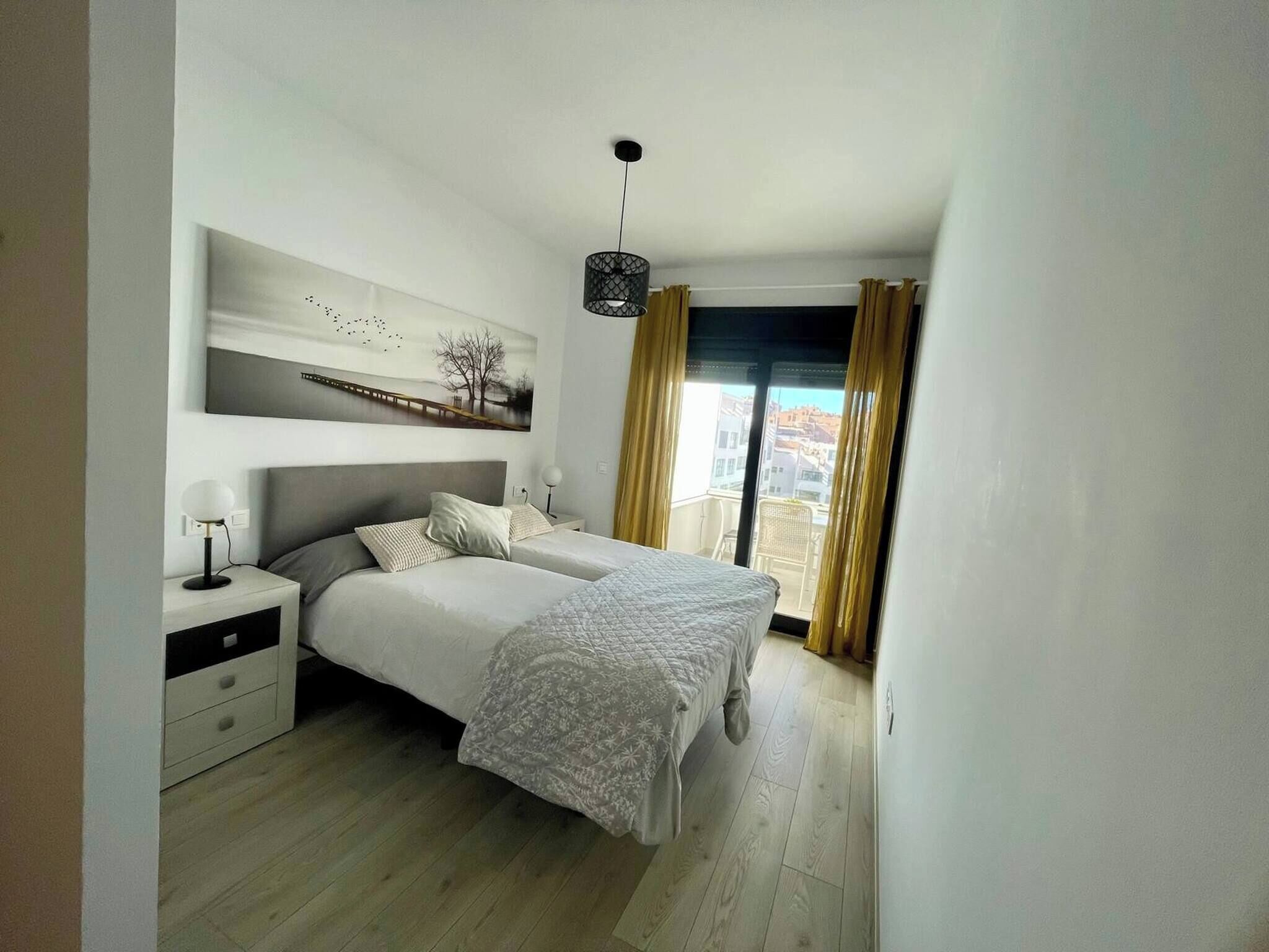 A bedroom with a bed, bedside tables, a lamp, a painting, and a view through a window.