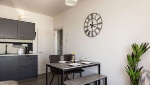 A modern kitchen with dark cabinets, a dining table set for two, and a large wall clock.