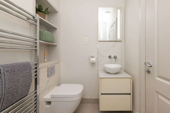 A compact bathroom with a toilet, a sink, a towel rack, and a mirror. - Seafront Apartment With Balcony Panoramic Views (Bognor Regis)