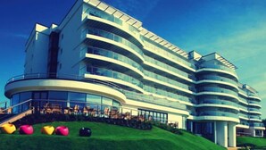 A modern multi-story hotel with a curved facade, large windows, and a grassy area with colorful spherical decorations.