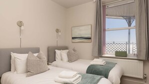 A bedroom with two beds, a window with a view, and a painting on the wall.