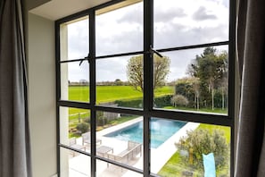 A window with a view of a swimming pool and a green landscape. - Chic Harbour Retreat for 10 With Pool (Chichester)