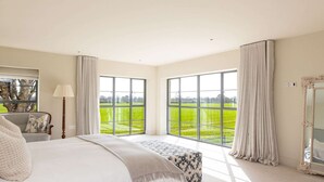 A bedroom with a large bed, a chair, a lamp, a mirror, and a view of a green landscape through large windows. - Chic Harbour Retreat for 10 With Pool (Chichester)