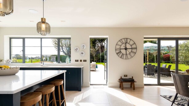 A modern kitchen with a large island, bar stools, a clock, and a view of the outdoors. - Chic Harbour Retreat for 10 With Pool (Chichester)