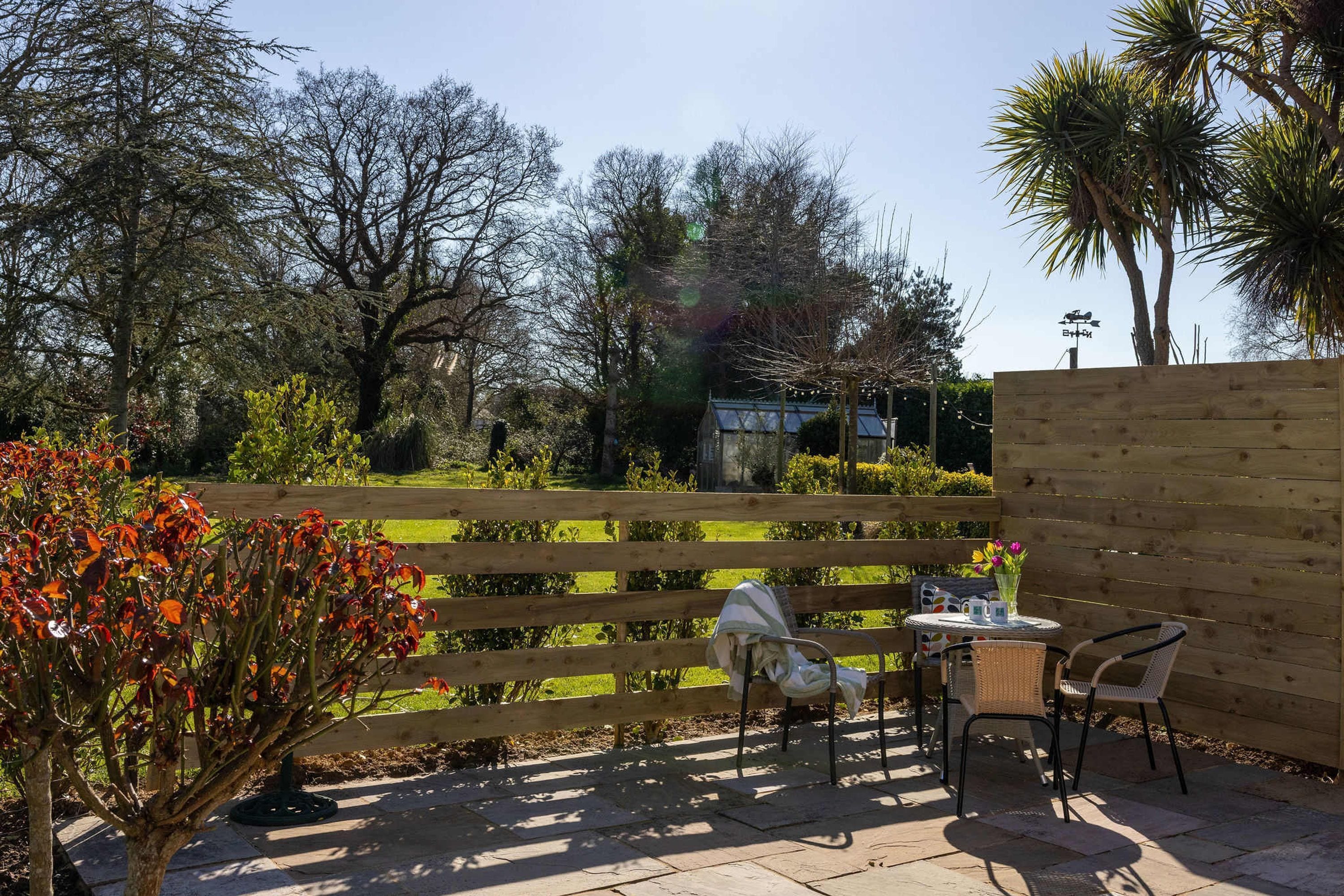 A patio with a wooden fence, a table with chairs, and a small garden area with trees and shrubs.