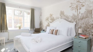 A bedroom with a large bed, a nightstand with books, a window with curtains, and a wall with a tropical mural. - Stylish One Bed Annexe Near Marina and Beaches (Chichester)