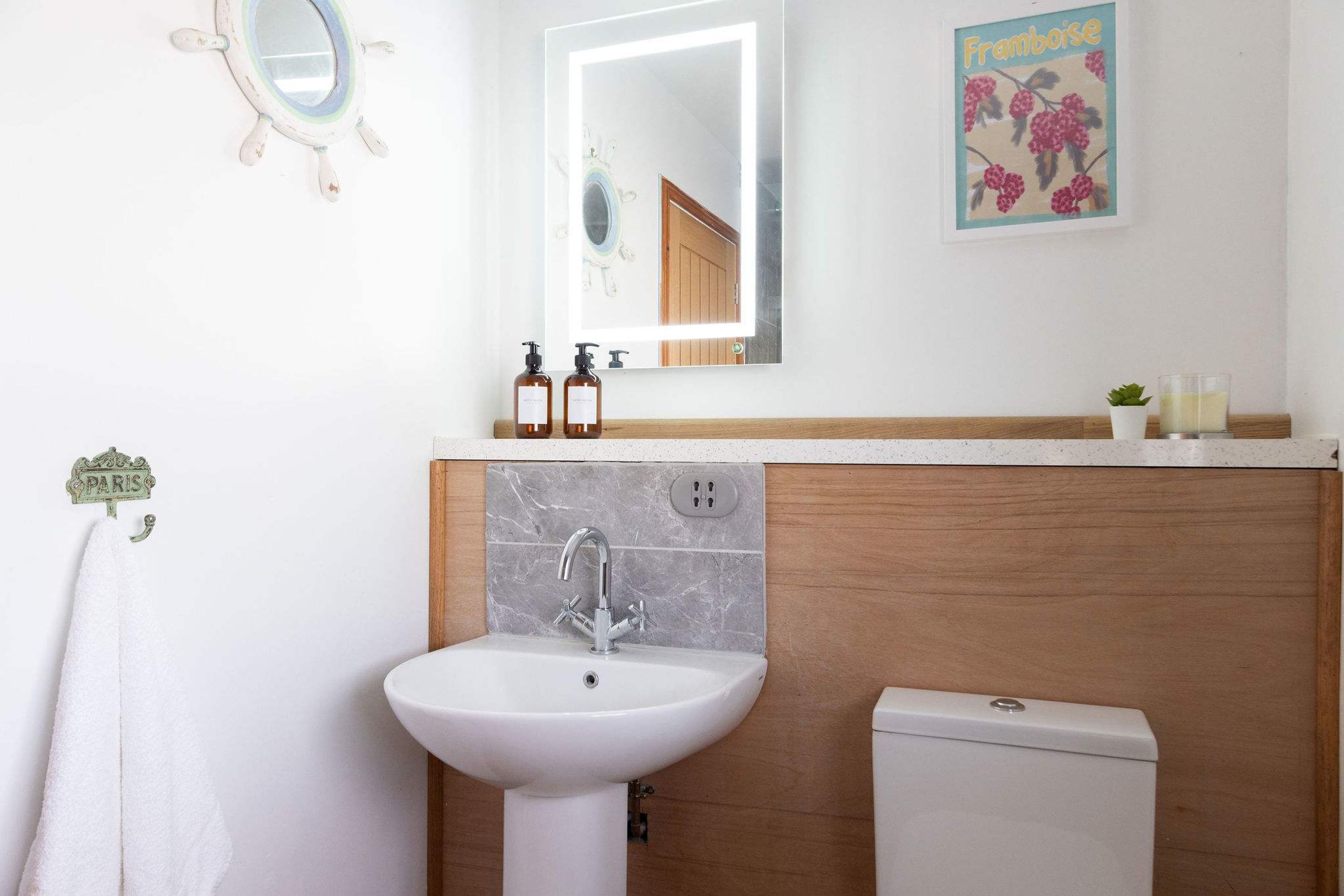 A bathroom with a white sink, a mirror, a toilet, and a wall-mounted shelf with toiletries.